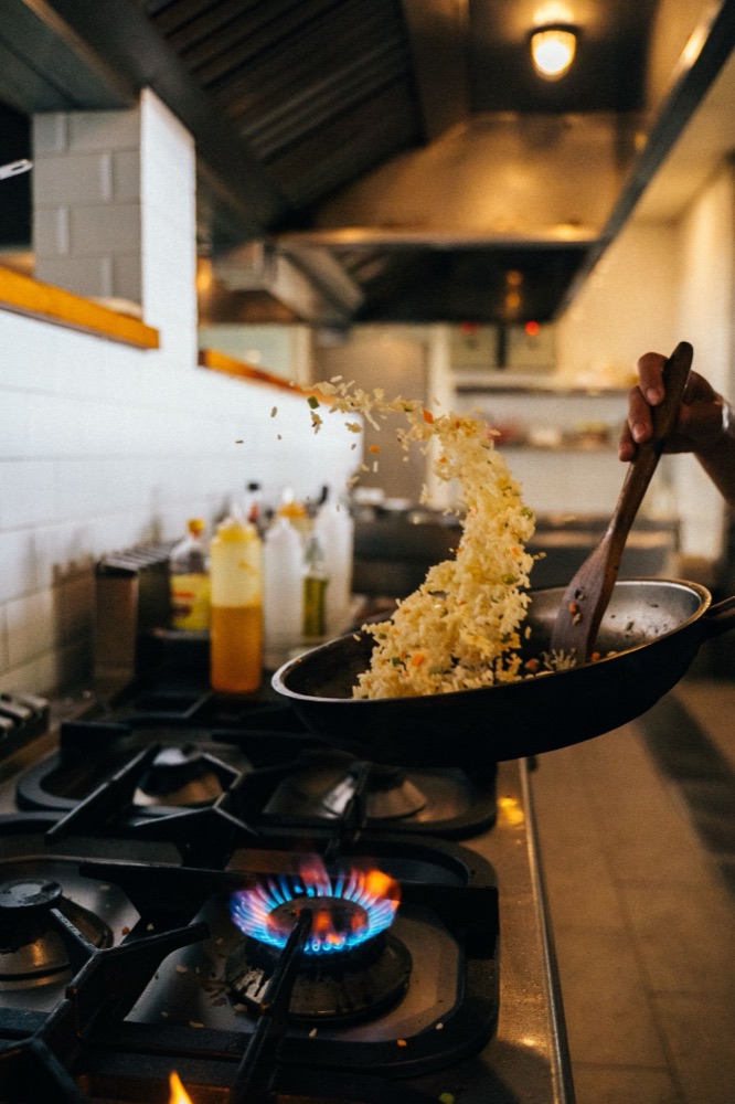 Chef tossing rice in a flaming pan on a restaurant line