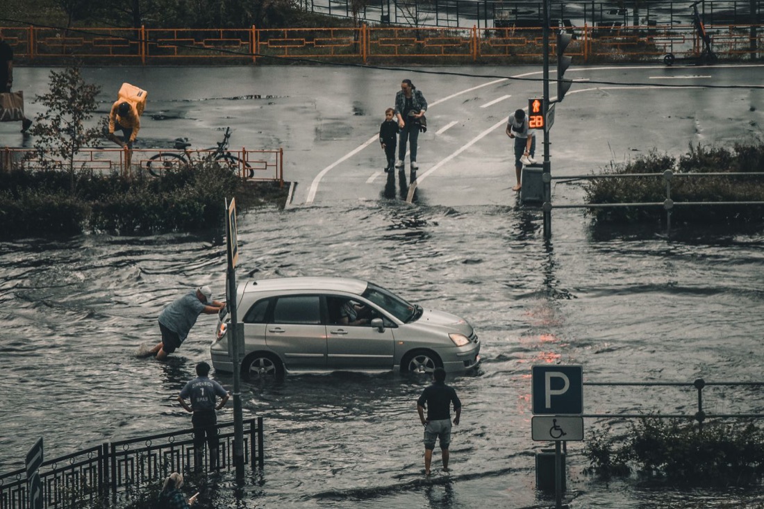 Car stalled in a flooded street as people wade through the water